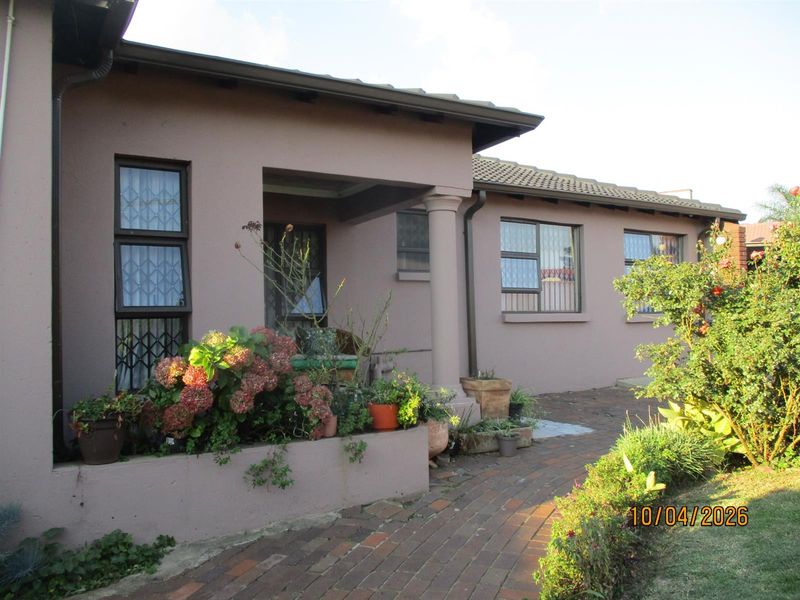 Exterior view of the house featuring a covered entrance porch, brick paved pathway, and established garden beds.