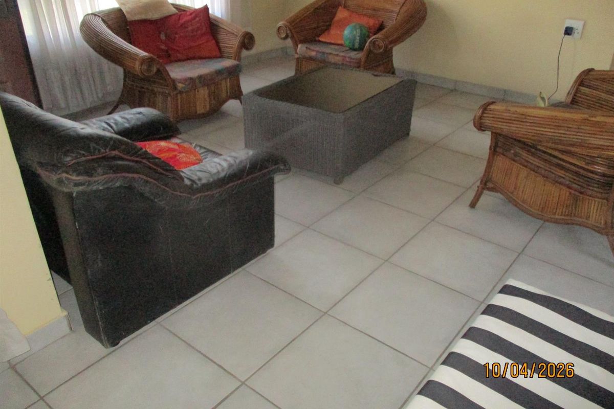 A living room area featuring neutral floor tiles and large windows with sheer curtains, providing a functional and well-lit space.