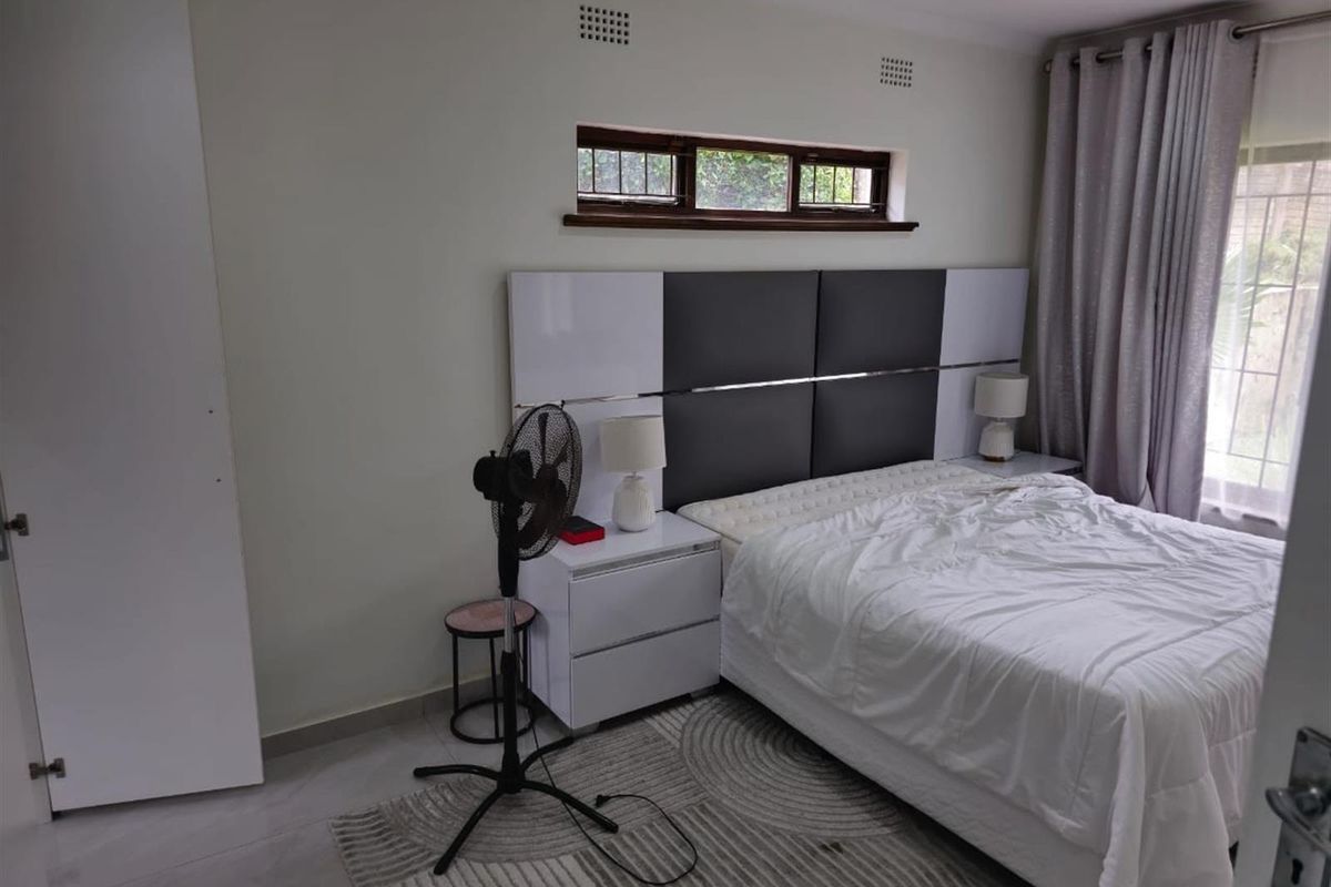 A well-maintained bedroom featuring a modern built-in headboard, tiled flooring, and a built-in cupboard, offering a clean and functional living space.