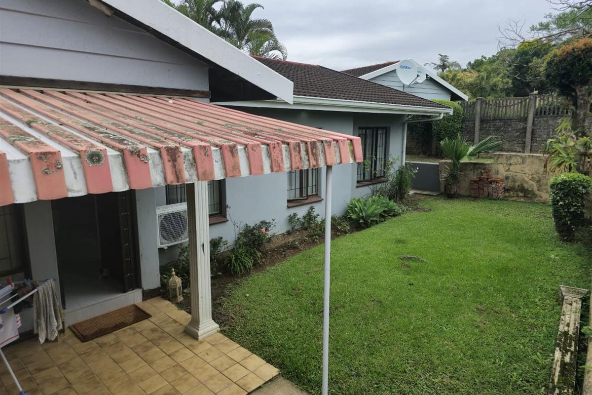 Rear view of the townhouse featuring a tiled patio with a weathered awning, a small lawn area, and a retaining wall.