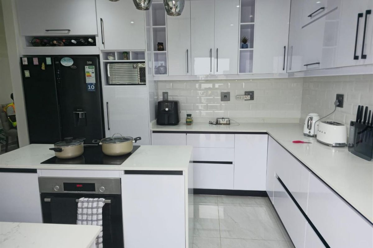 Modern kitchen featuring white high-gloss cabinetry, stone countertops, subway tile backsplash, and integrated appliances including an electric hob and built-in oven.
