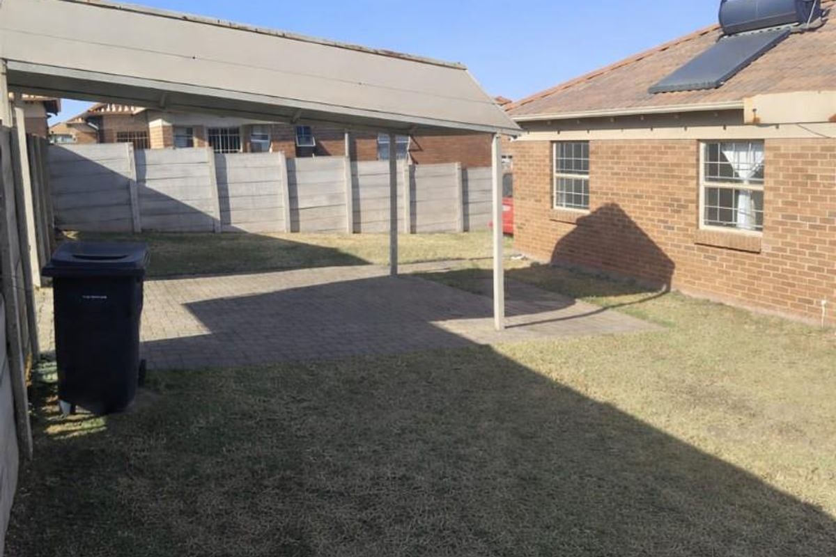 A rear garden area featuring a paved patio with a covered structure, brick exterior wall, and a solar water heating system on the roof.