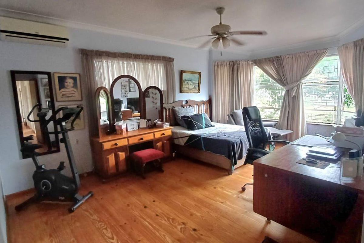 Spacious bedroom featuring polished timber flooring, a ceiling fan, and a wall-mounted air conditioning unit, offering a comfortable and functional living space.