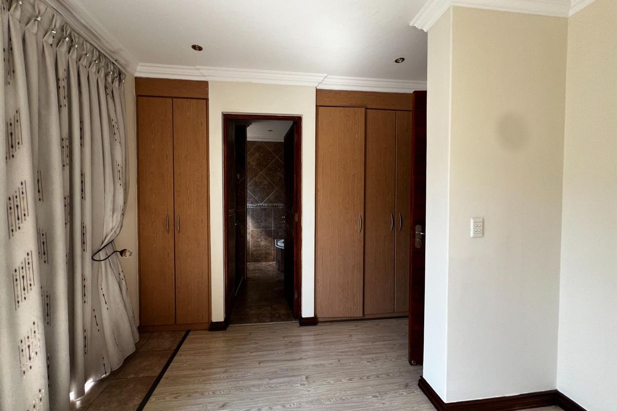 Bedroom featuring built-in wooden cupboards, laminate flooring, and direct access to an en-suite bathroom.