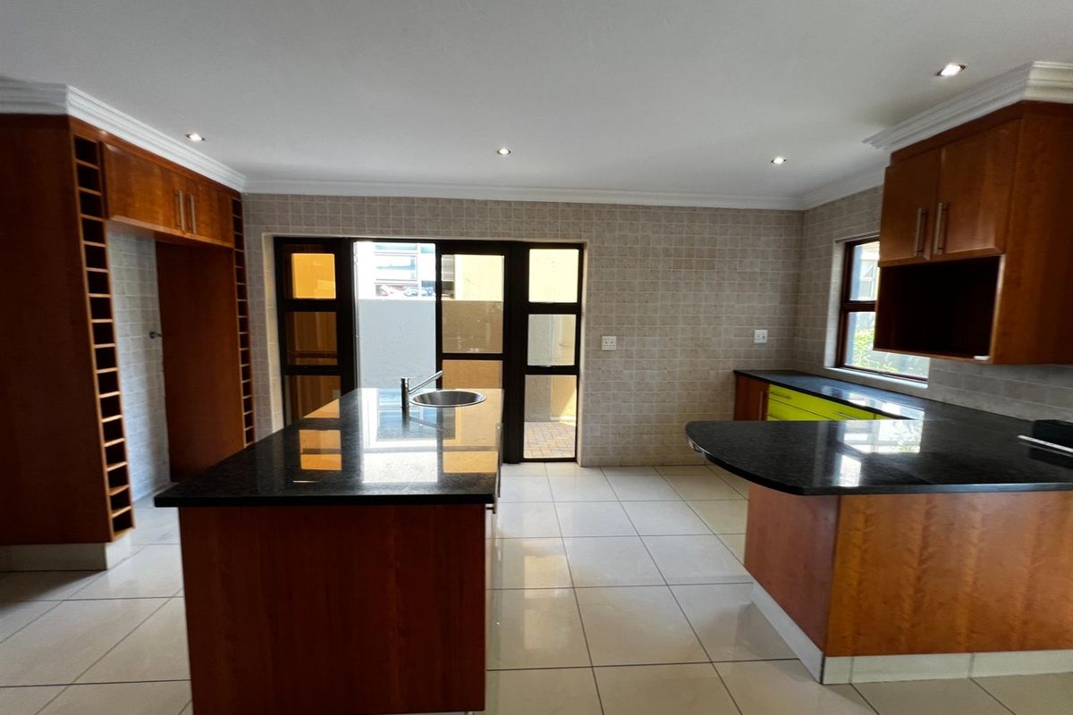 Spacious kitchen featuring dark granite countertops, a central island with a prep sink, and extensive wooden cabinetry with integrated storage.