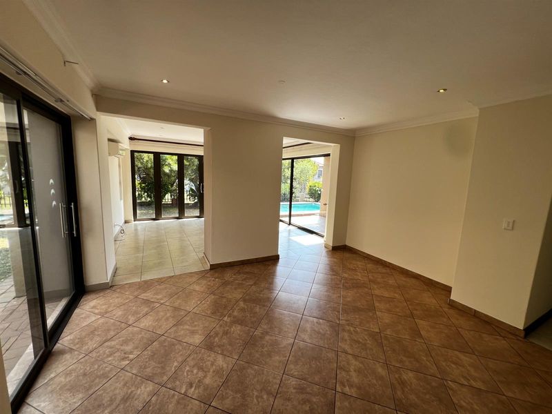 Spacious open-plan living area featuring tiled flooring, recessed downlighting, and large sliding glass doors providing direct access to the outdoor pool and garden area.