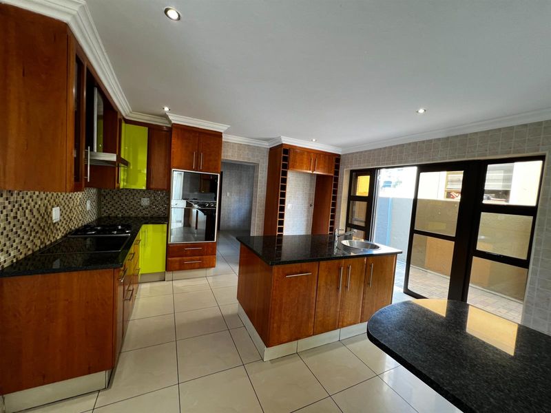 Spacious kitchen featuring wooden cabinetry with lime green accents, granite countertops, a central island with sink, and direct access to an outdoor patio area.