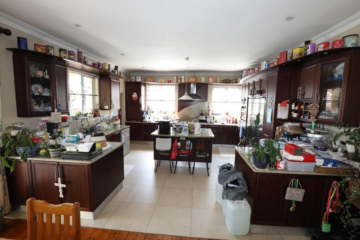 Spacious kitchen featuring dark wood cabinetry, stone countertops, a central island, and integrated stainless steel appliances with tiled flooring.