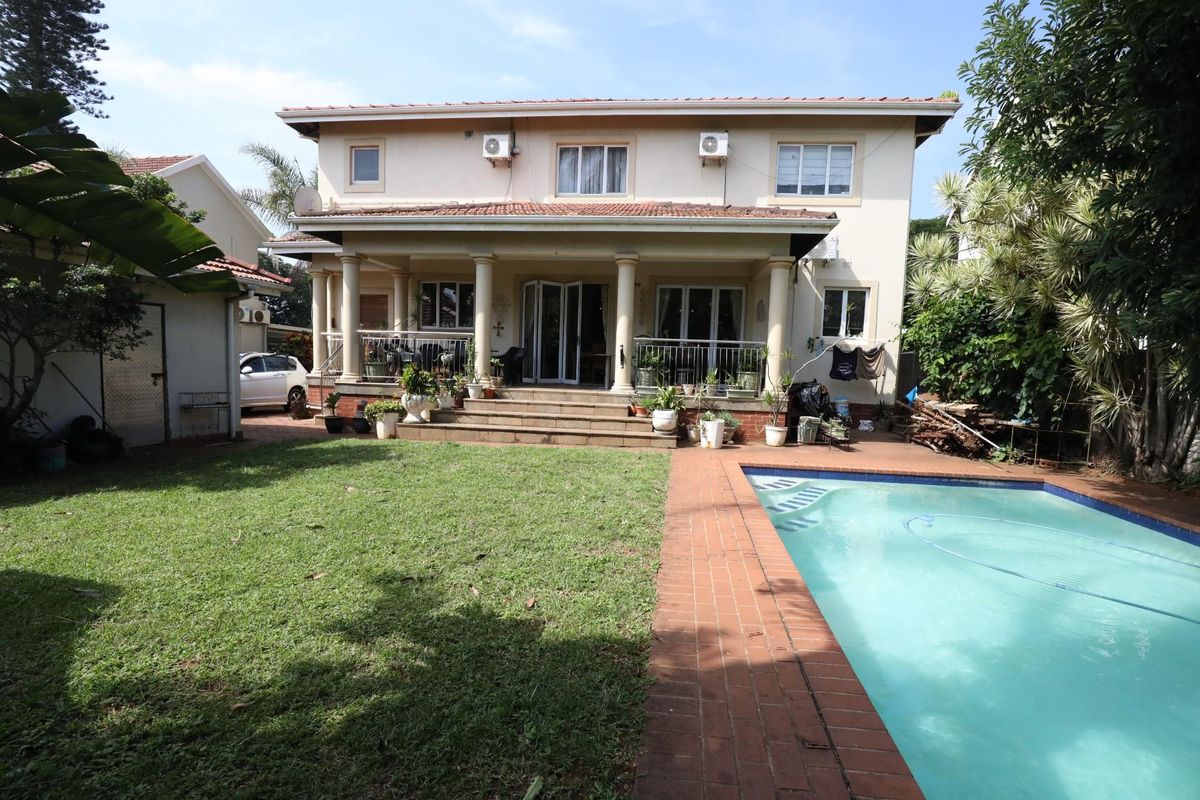 Rear view of a two-story house featuring a covered patio, swimming pool, and a spacious garden area.