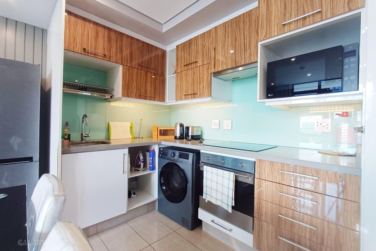 Modern kitchen featuring wood-grain cabinetry, glass splashbacks, integrated appliances, and sleek stone countertops in a compact, efficient layout.