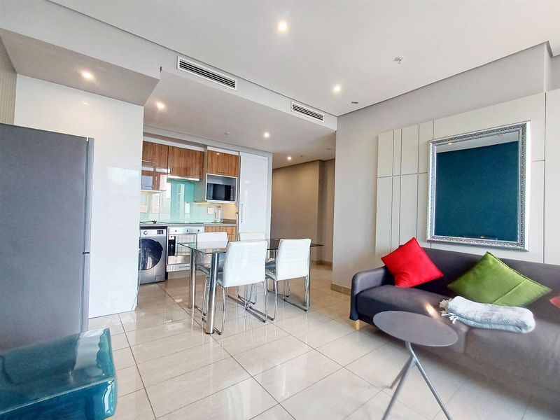 Modern open-plan living area featuring a sleek kitchen with built-in appliances, tiled flooring, and recessed lighting, creating a bright and functional space.