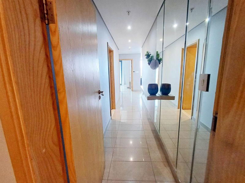 A bright, modern hallway featuring polished tiled flooring, recessed downlighting, and a full-length mirrored wall panel that enhances the sense of space.