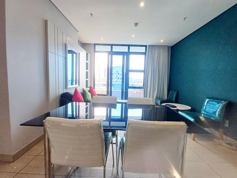 A modern living and dining area featuring tiled floors, a decorative feature wall, and large glass doors providing natural light and access to the balcony.