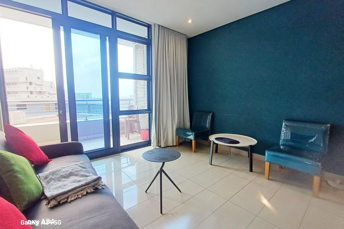 A bright living room featuring large glass sliding doors leading to a balcony, tiled flooring, and a bold blue accent wall.