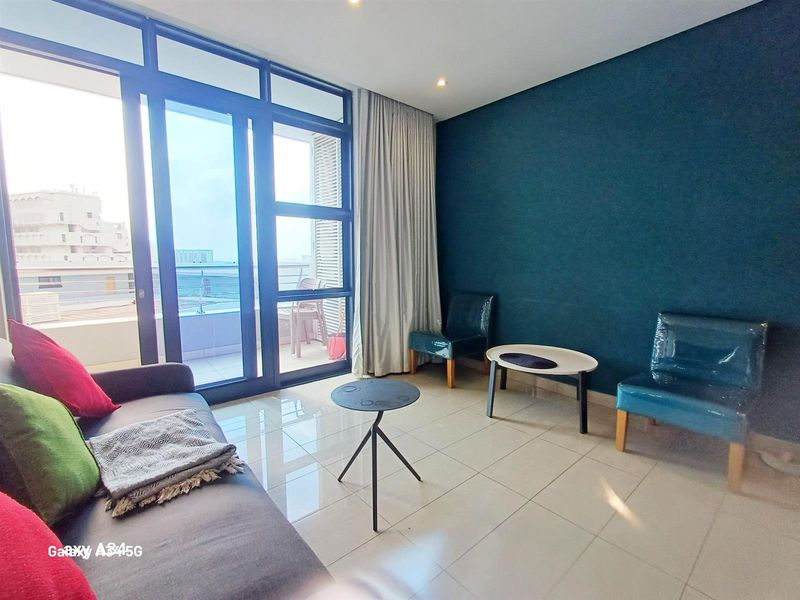 A bright living room featuring large glass sliding doors leading to a balcony, tiled flooring, and a bold blue accent wall.
