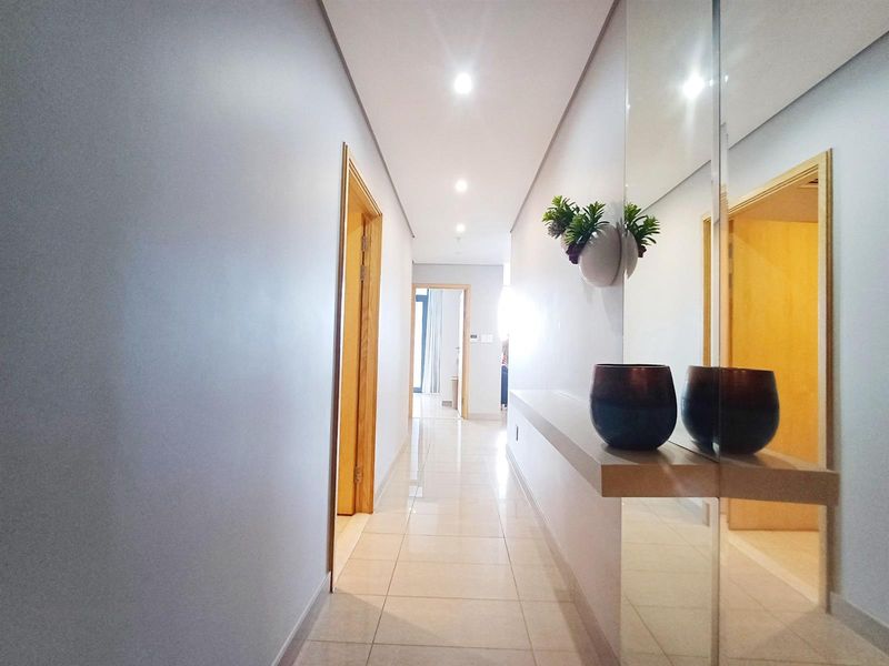 A bright, modern hallway featuring polished tiled flooring, recessed downlighting, a built-in floating shelf, and a large wall-mounted mirror.