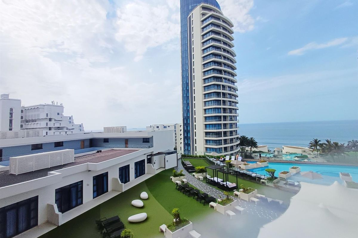 Aerial view of a modern high-rise apartment complex featuring a swimming pool, landscaped garden areas, and ocean views.