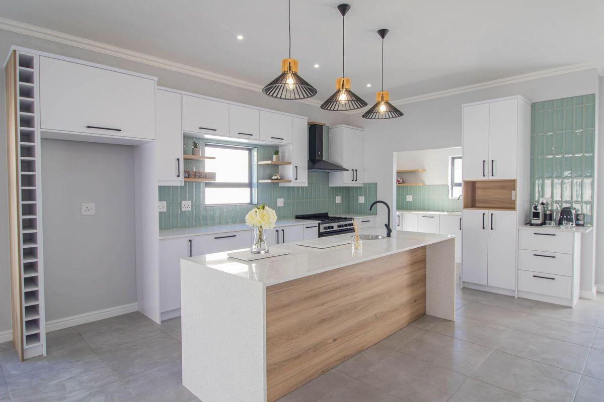 Modern kitchen featuring white cabinetry, a central island with stone countertop, light wood accents, green subway tile backsplash, and integrated stainless steel appliances.