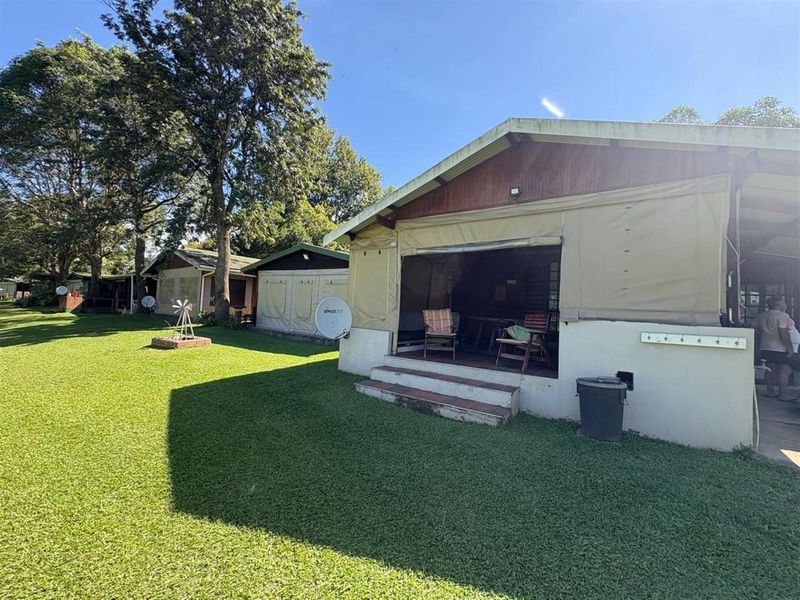 Rear view of a holiday accommodation unit featuring a covered patio area with roll-up canvas blinds and a surrounding lawn.