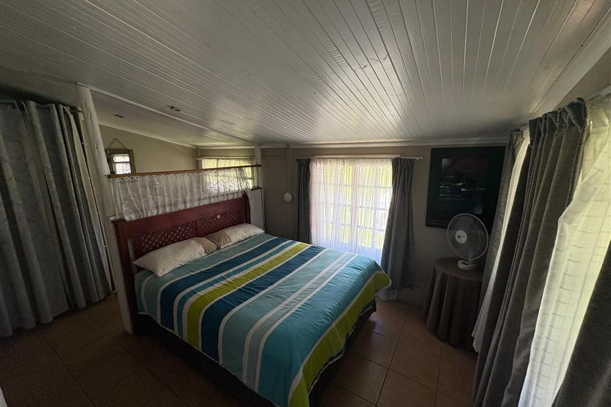 A bedroom featuring tiled flooring and a timber panelled ceiling, offering a functional space with natural light from the window.