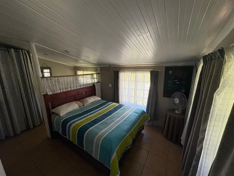 A bedroom featuring tiled flooring and a timber panelled ceiling, offering a functional space with natural light from the window.