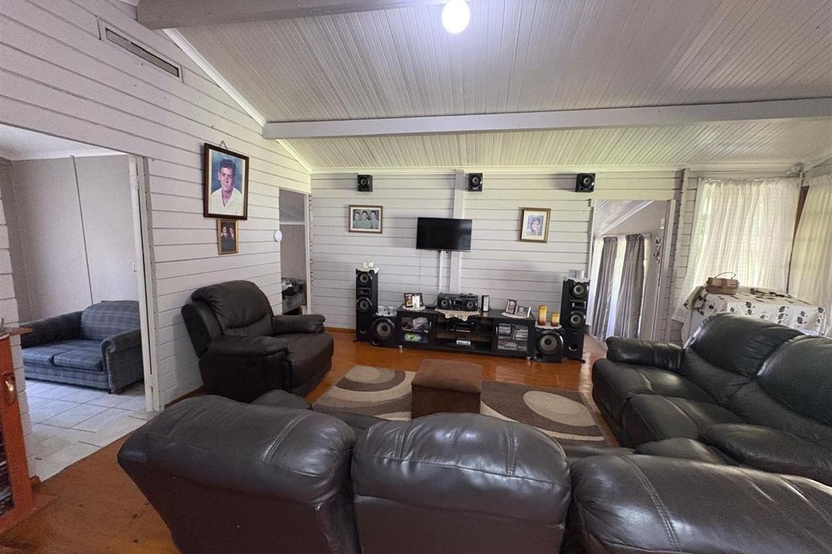 Spacious living room featuring timber wall cladding, exposed ceiling beams, and warm timber flooring, creating a cozy and traditional atmosphere.