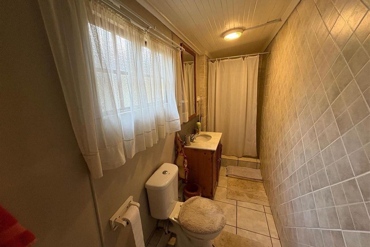 A compact bathroom featuring a vanity basin, toilet, and shower area with tiled walls and a tongue and groove ceiling.