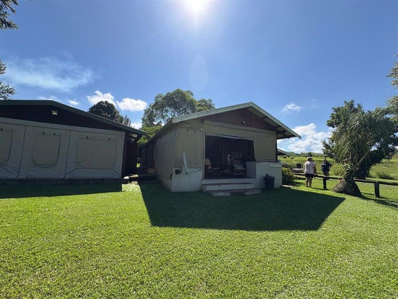 Rear view of a canvas-walled holiday accommodation unit featuring a covered patio area and surrounding lawn.