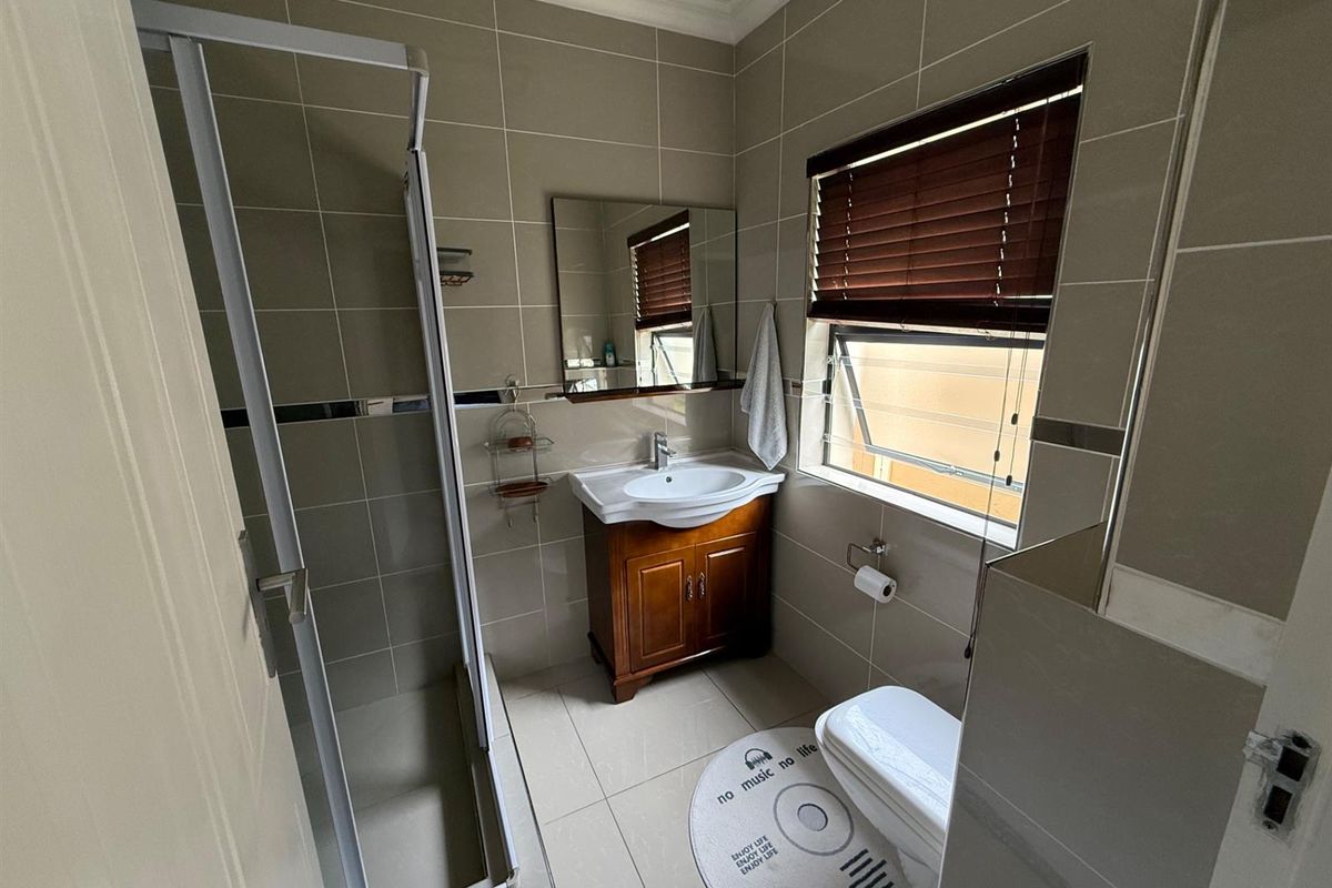 A well-maintained bathroom featuring a shower enclosure, vanity cabinet with basin, and neutral wall tiling.