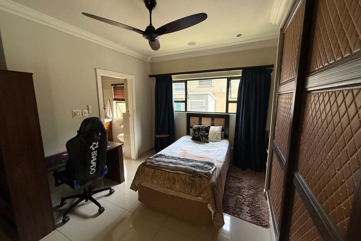 A functional bedroom featuring tiled floors, a ceiling fan, built-in cupboards, and an attached en-suite bathroom.