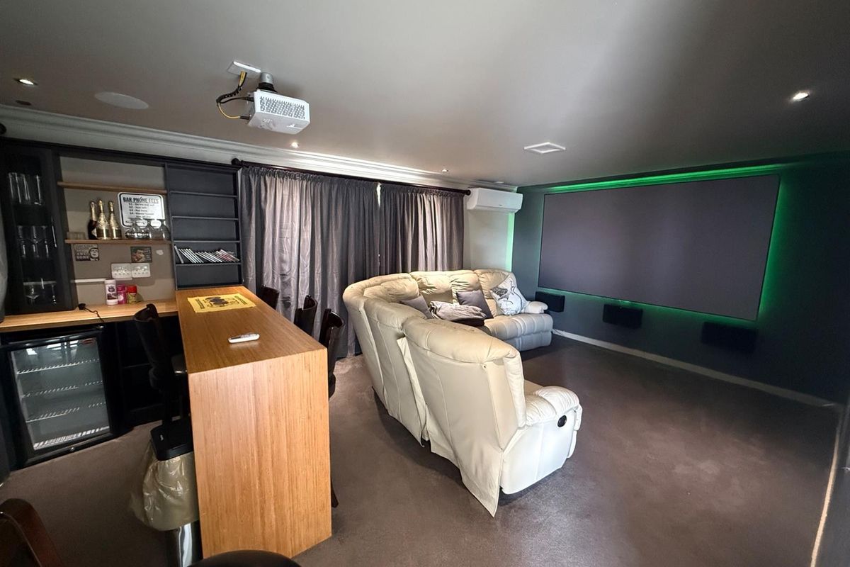 A dedicated home cinema room featuring a large projection screen, integrated sound system, projector, and a built-in bar area for entertainment.