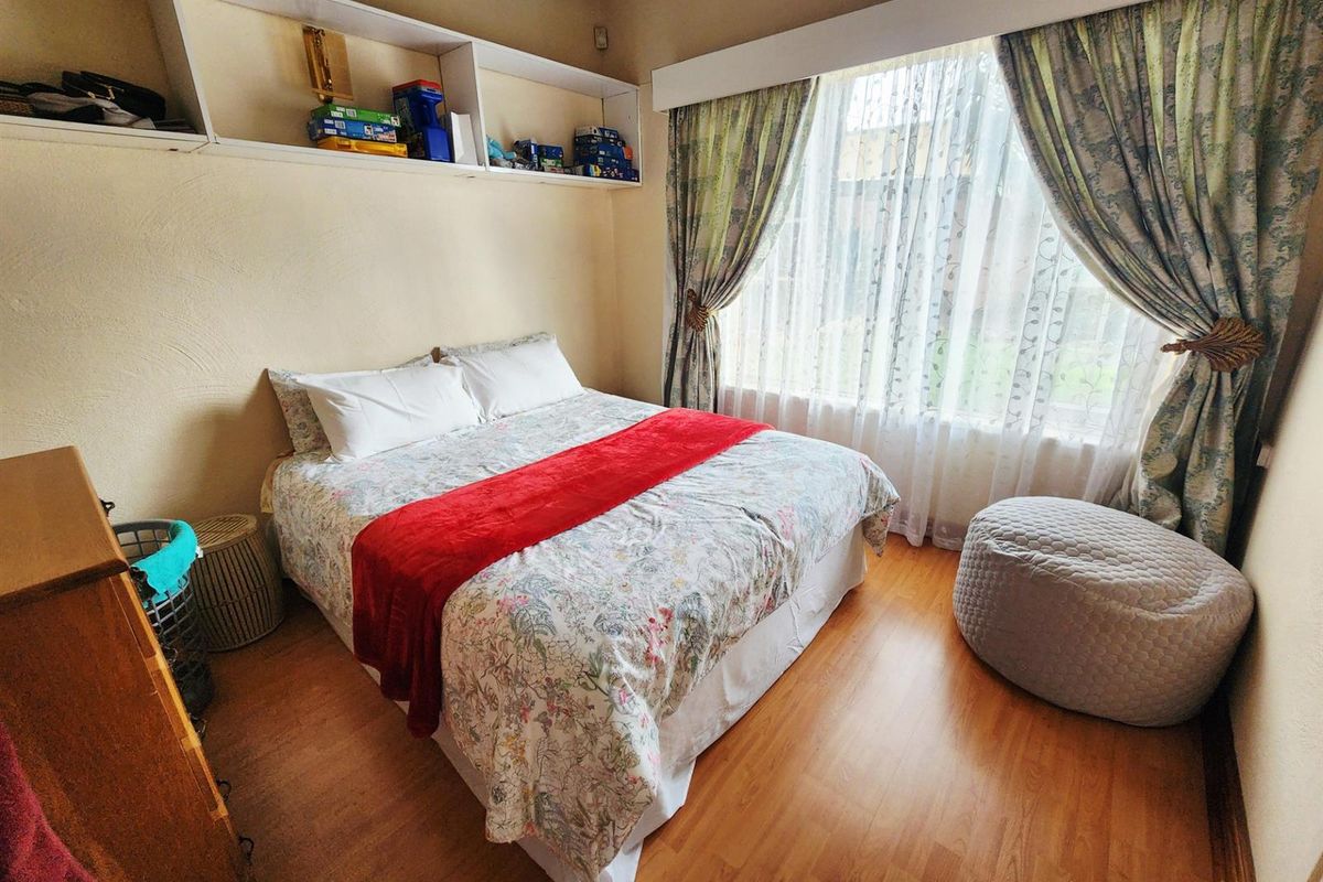 A cozy bedroom featuring wood-look laminate flooring, built-in wall shelving, and a large window with curtains.