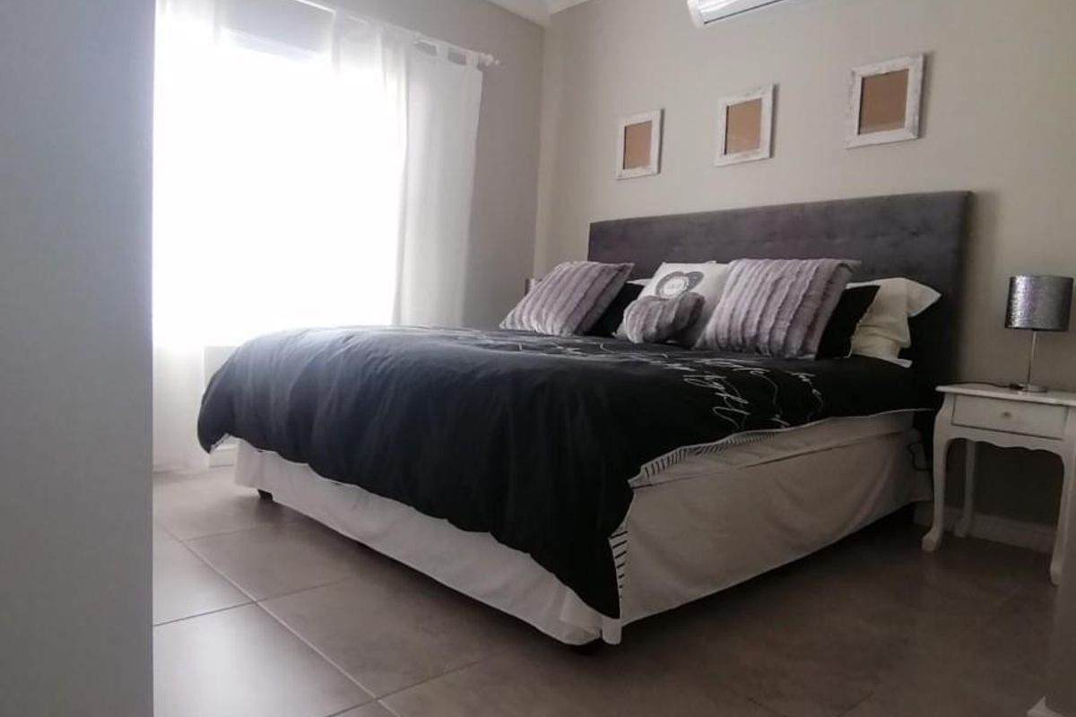 A well-maintained bedroom featuring tiled flooring, a vaulted ceiling with exposed beams, and a wall-mounted air conditioning unit.