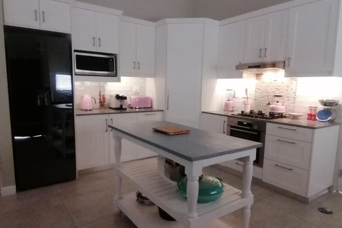 Modern kitchen featuring white cabinetry, stone countertops, built-in oven, gas hob, extractor fan, and a central island under a vaulted ceiling.