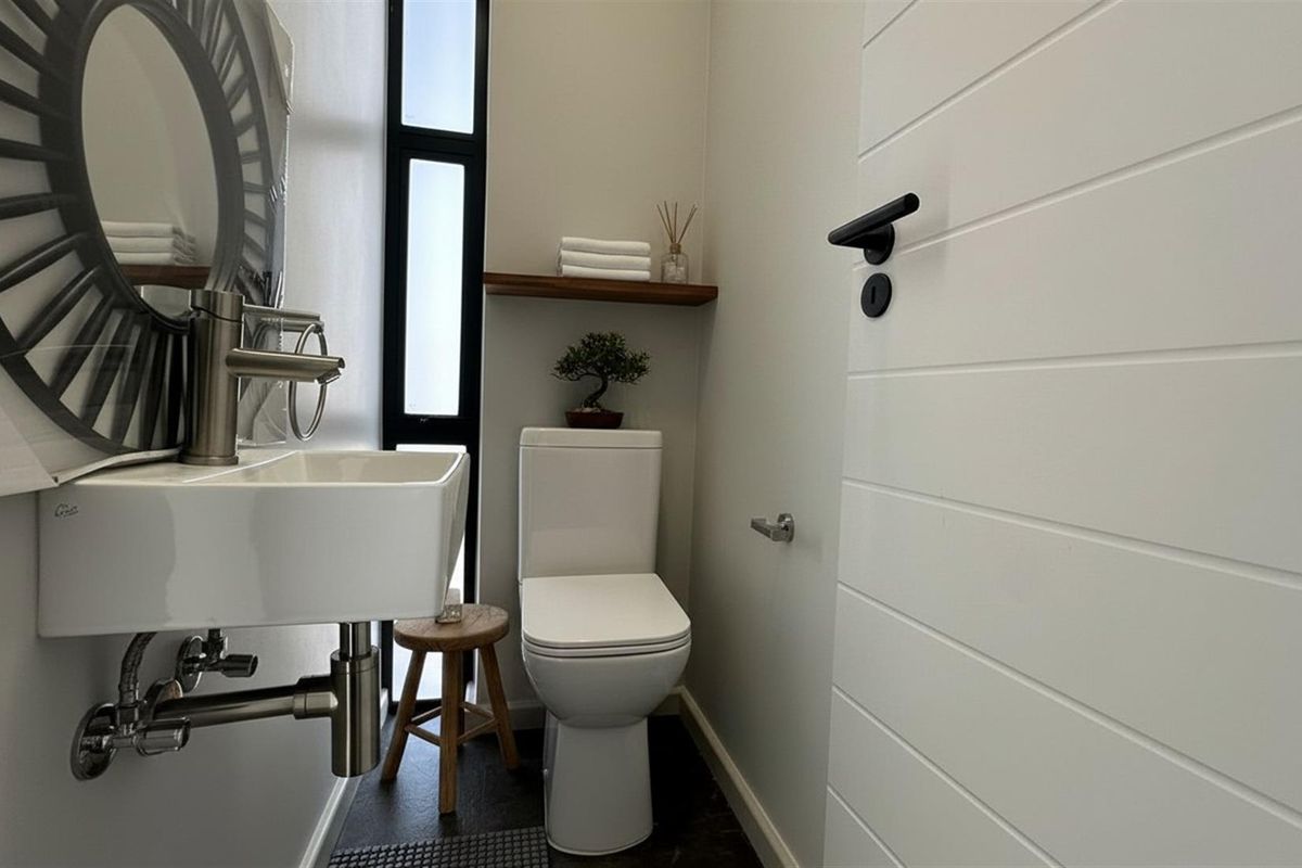 A modern, compact guest bathroom featuring a wall-mounted basin, sleek toilet, and vertical window, finished with clean lines and contemporary fixtures.