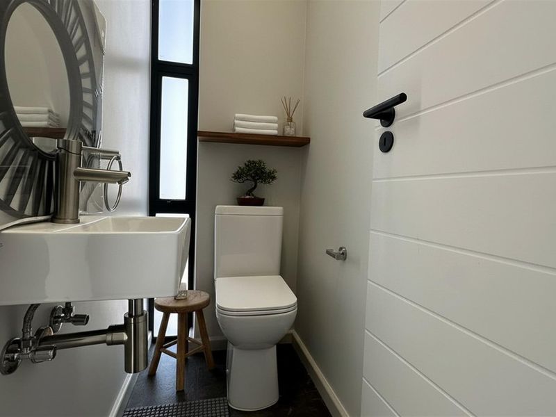 A modern, compact guest bathroom featuring a wall-mounted basin, sleek toilet, and vertical window, finished with clean lines and contemporary fixtures.