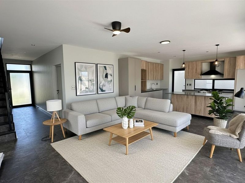 Modern open-plan living area featuring a contemporary kitchen with wood-finish cabinetry, a central island, and a sleek staircase leading to the upper level.