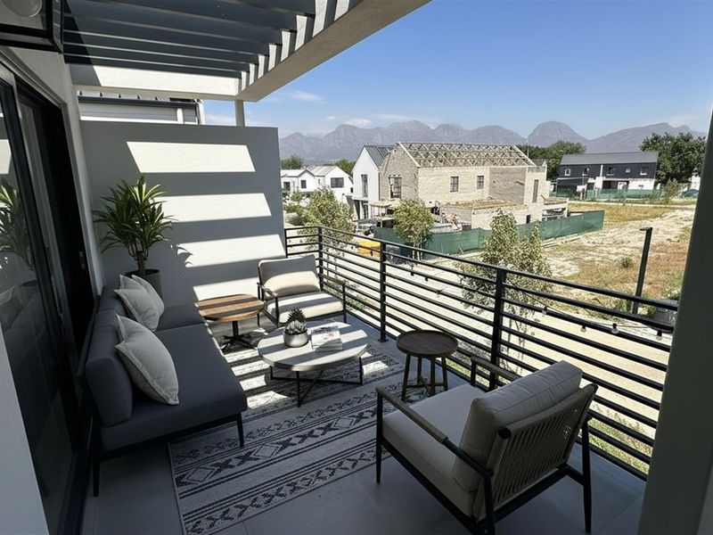 A modern covered balcony featuring a slatted pergola roof, sleek metal railings, and tiled flooring, offering views of the surrounding neighbourhood and mountains.