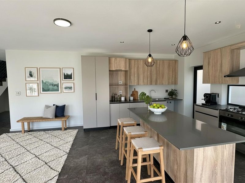 Modern open-plan kitchen featuring wood-grain cabinetry, stone countertops, a central island, and a built-in gas stove with an extractor fan.