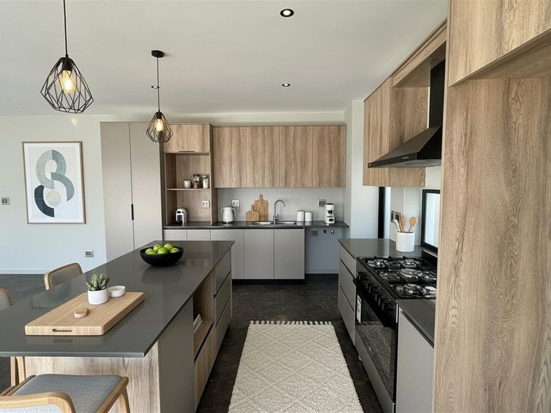 Modern open-plan kitchen featuring wood-grain cabinetry, a central island with stone countertop, built-in gas hob, and integrated extractor fan.