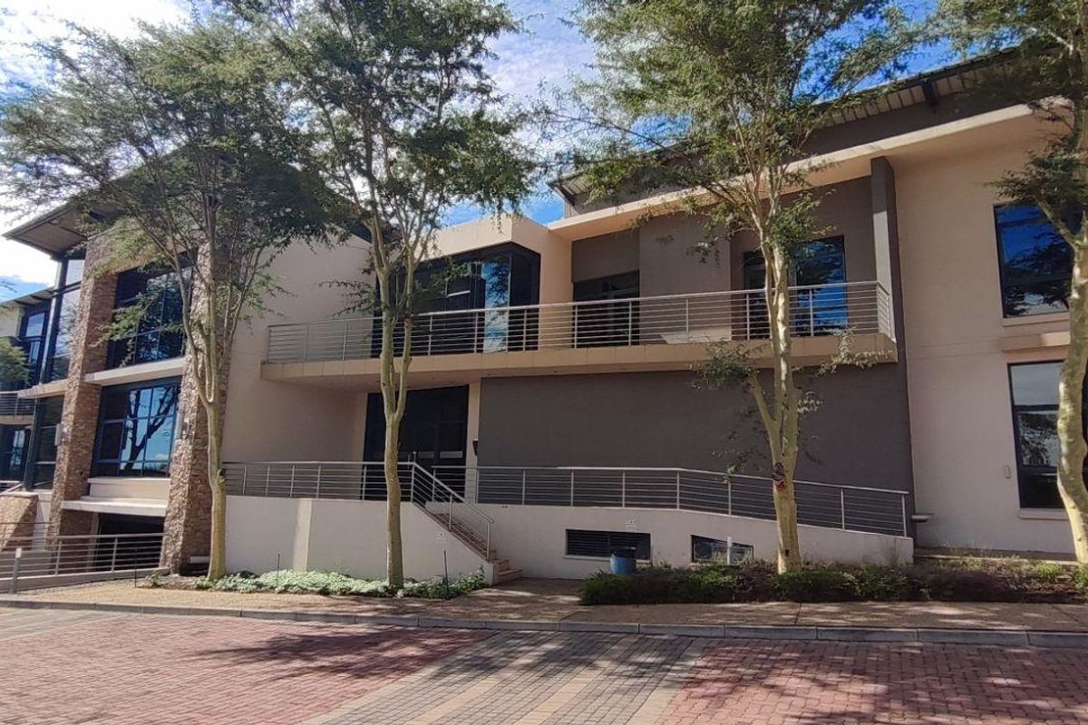 Modern commercial building exterior featuring a multi-level facade with large glass windows, metal railings, and paved driveway access.