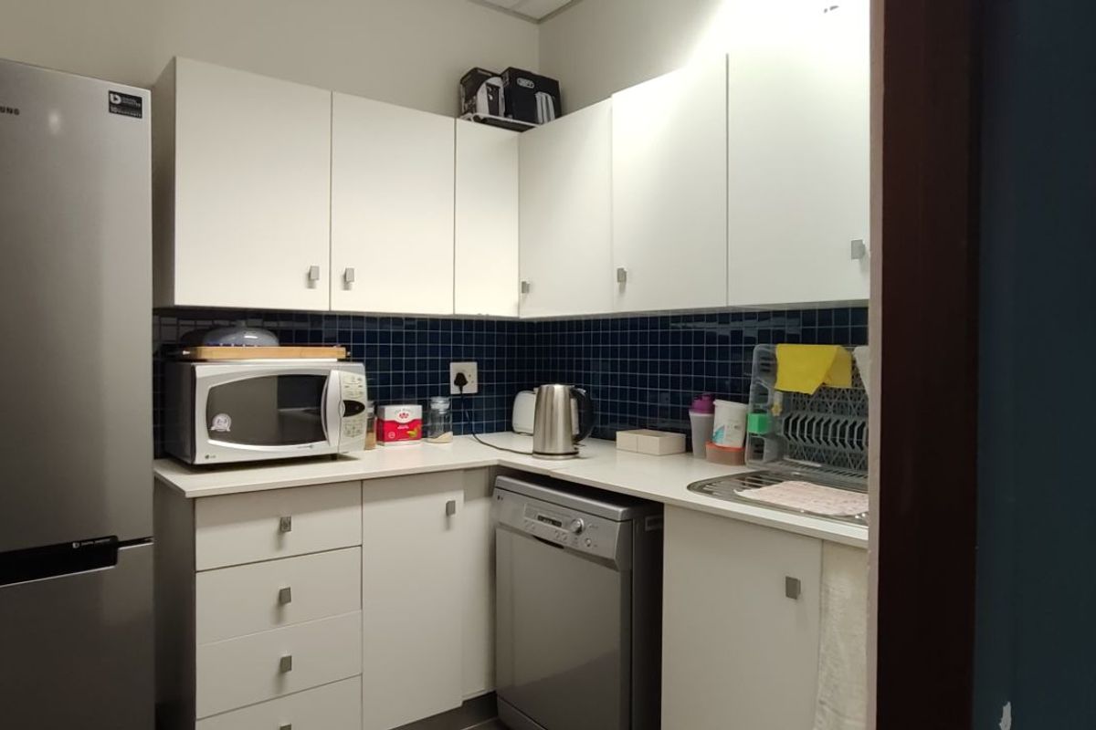 Compact kitchenette featuring white cabinetry, dark blue tiled backsplash, stainless steel sink, and integrated space for appliances.
