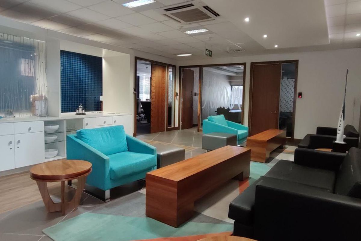 A modern commercial office reception or lounge area featuring built-in cabinetry, recessed ceiling lighting, and glass-paneled office doors.