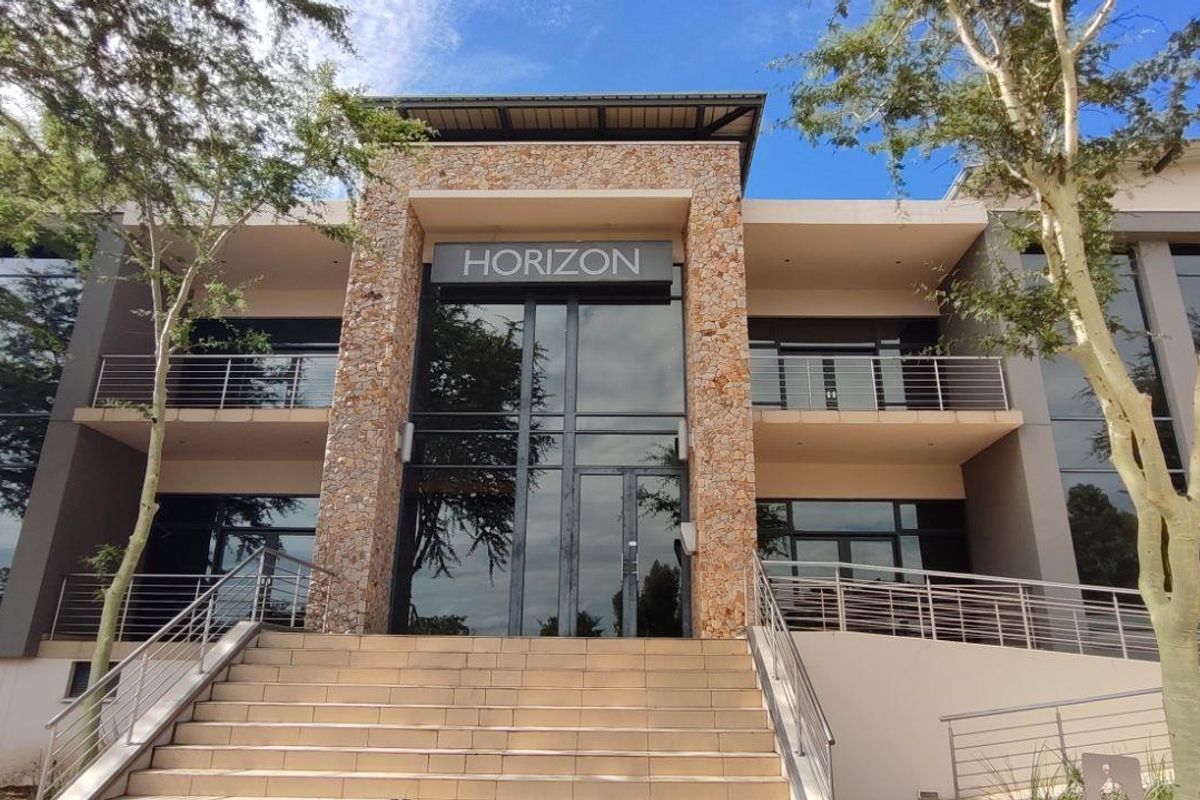 Modern commercial building facade featuring stone cladding, large glass curtain walls, and elevated entrance stairs with stainless steel railings.