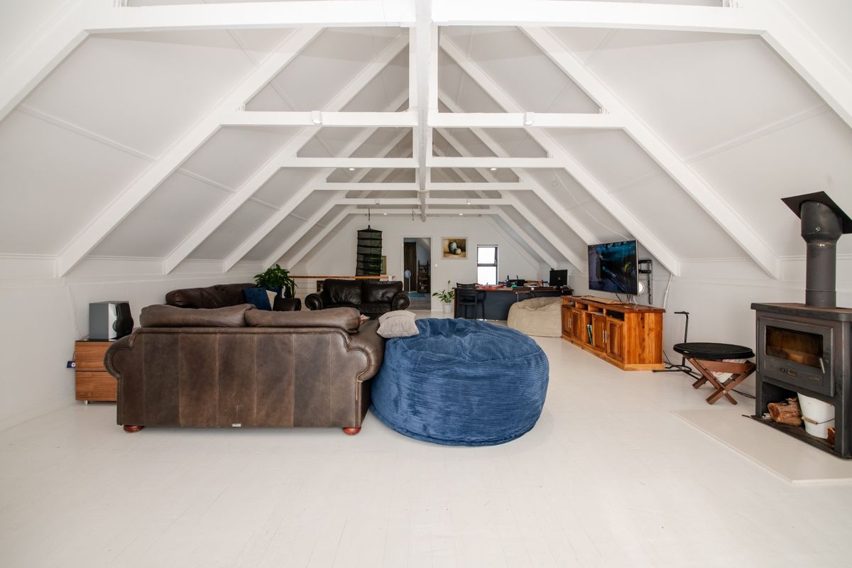 Spacious attic-style living room featuring exposed vaulted timber beams, white painted flooring, and a built-in wood-burning fireplace.