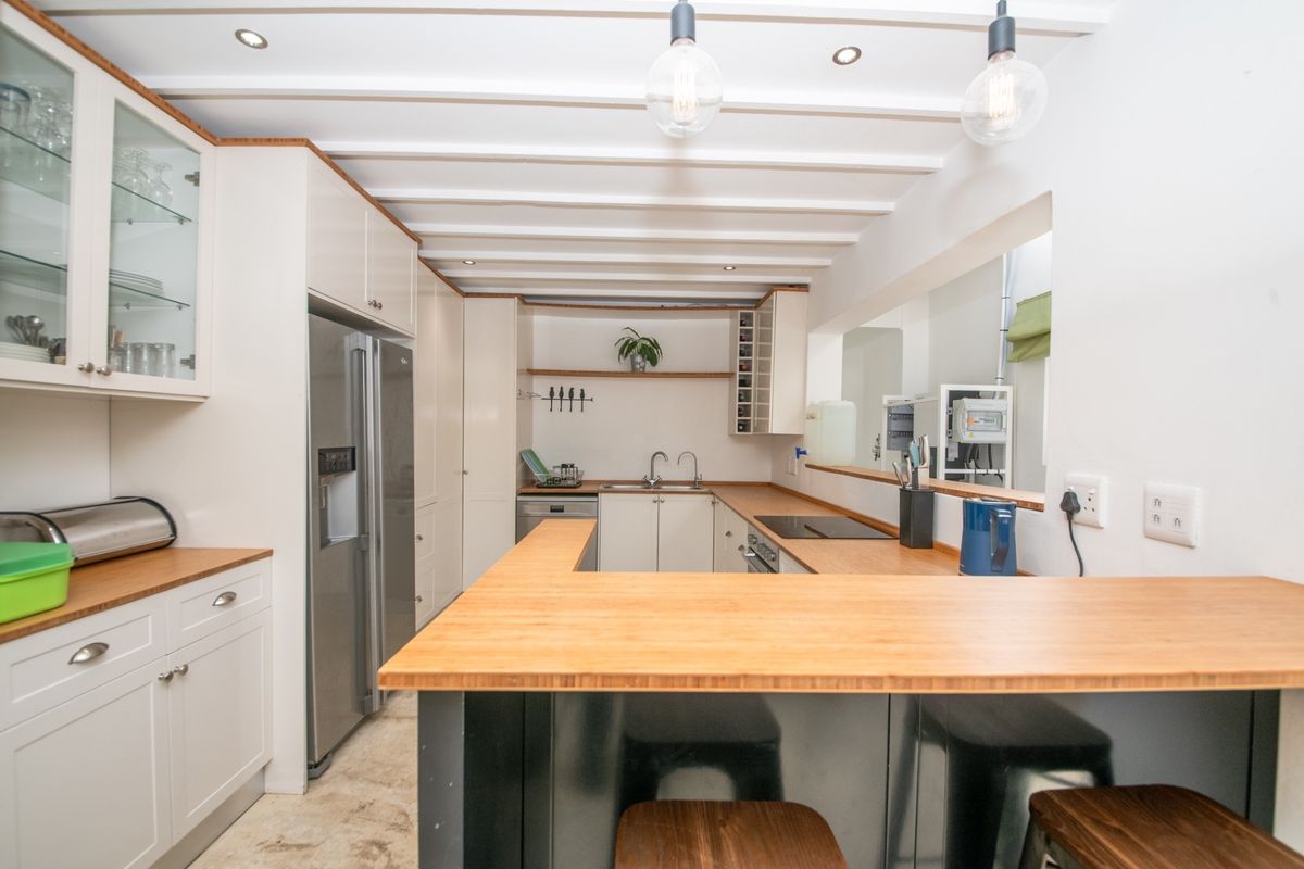 Modern kitchen featuring light cabinetry, wooden countertops, a breakfast bar, integrated appliances, and exposed beam ceiling detail.
