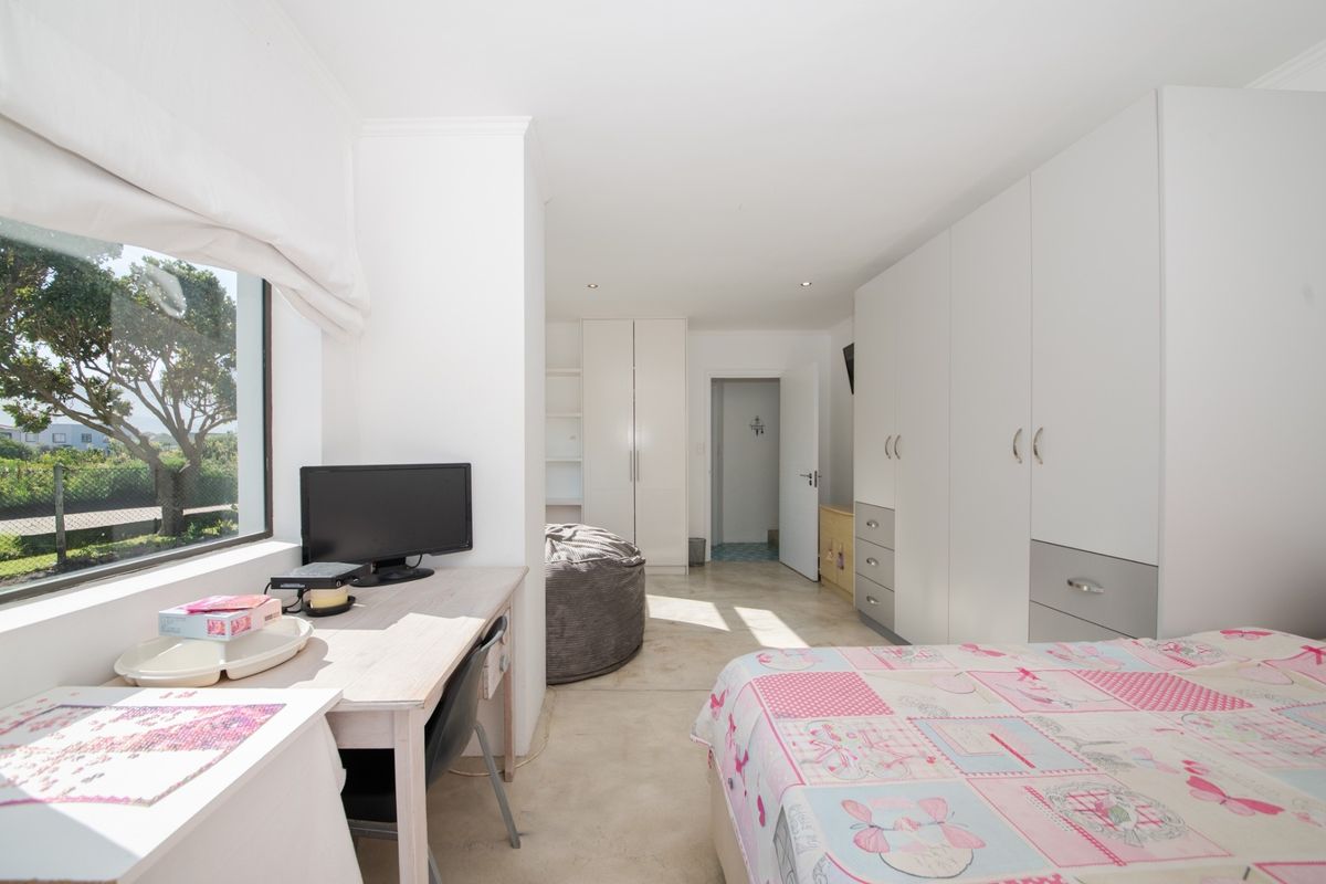 A bright bedroom featuring extensive built-in cabinetry, polished concrete flooring, and large windows providing natural light and garden views.