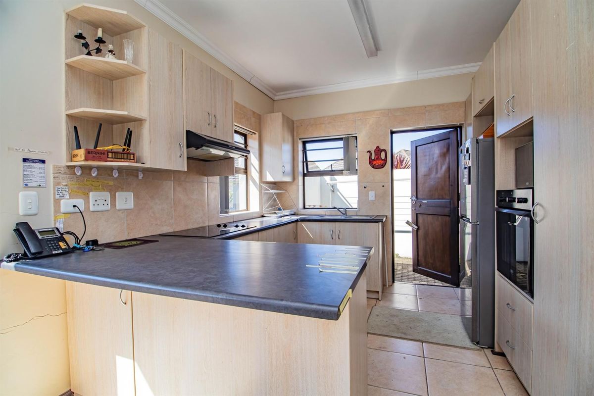 A functional kitchen featuring light wood-finish cabinetry, dark laminate countertops, built-in oven, extractor fan, and direct access to an outdoor area.