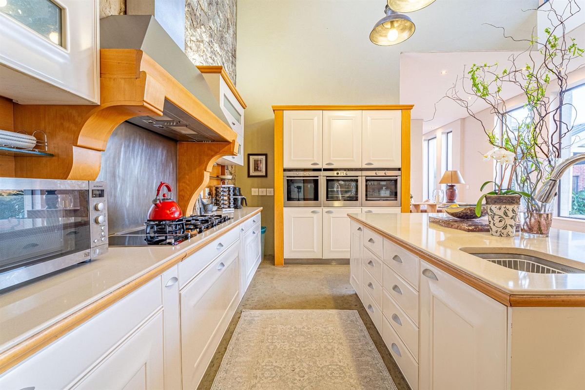 Spacious kitchen featuring white cabinetry, stone countertops, a central island with sink, and built-in triple ovens under a high vaulted ceiling.