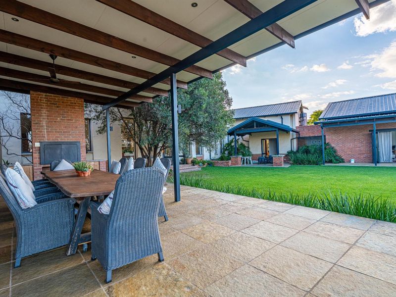 Spacious covered patio featuring a built-in brick fireplace, overlooking a well-maintained garden and rear building elevation.